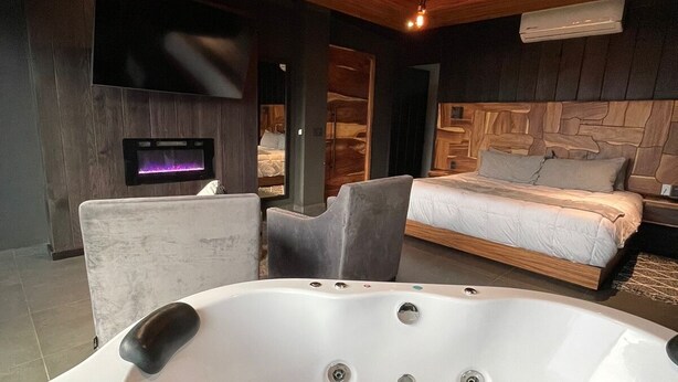 Un dormitorio moderno con una bañera grande, una cama y un televisor montado en la pared.