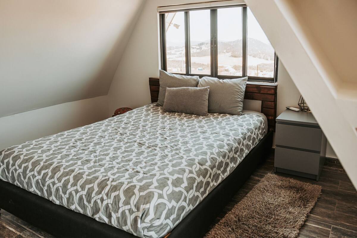 A bedroom with a bed, nightstands, a window, and a view of the outdoors.