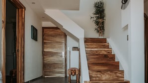 Un interior moderno con una escalera de madera, un pasillo que conduce a una puerta y un pequeño taburete.