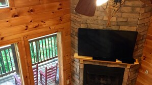 Interior acogedor de una cabaña con chimenea de piedra, televisor montado y techo de madera.