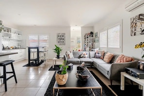 A modern living room with a grey sofa, a coffee table, and a dining area with a white table and chairs. - Relax & Unwind with Private Hot Tub in Rosebud (Rosebud)