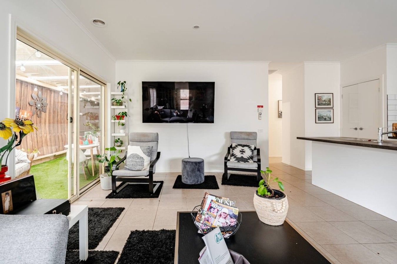 A modern living room with a flat-screen TV, two grey armchairs, a coffee table, and a small side table.