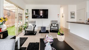 A modern living room with a flat-screen TV, two grey armchairs, a coffee table, and a small side table. - Relax & Unwind with Private Hot Tub in Rosebud (Rosebud)