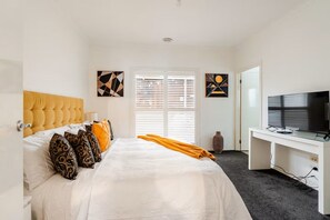 Quarto de hotel com cama, escrivaninha, televisão e obras de arte nas paredes.