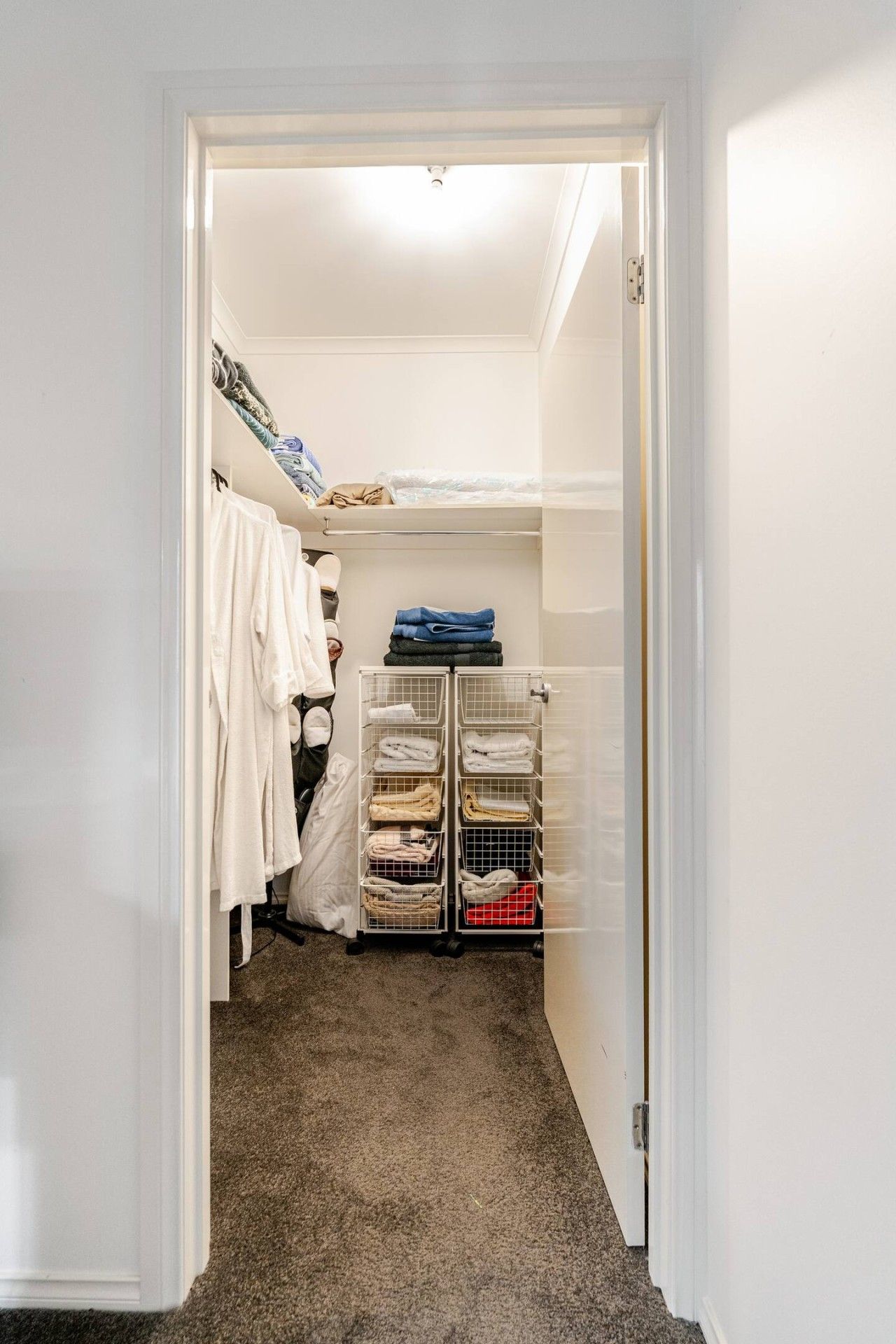 A walk-in closet with hanging clothes, a folded clothes rack, and a shoe rack.