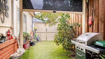 A backyard with a barbecue grill, a fire extinguisher, potted plants, and a wooden fence.