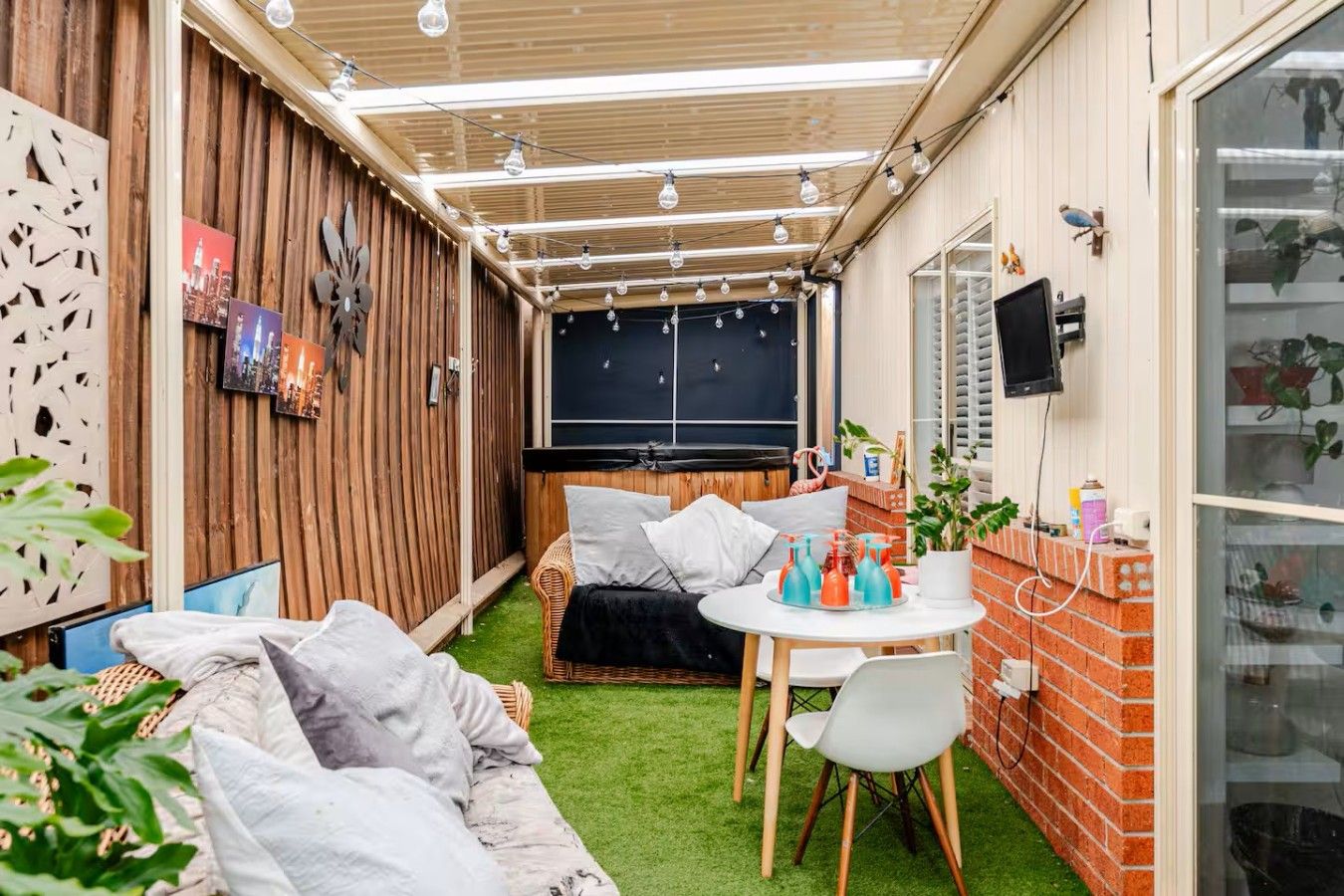 A cozy outdoor living area with a sofa, a dining table, and a TV screen.