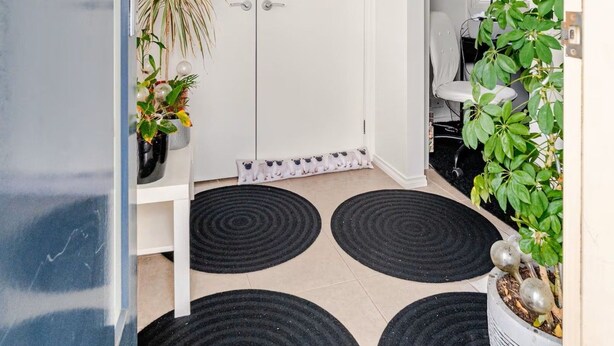 A hallway with a white door, a potted plant, and black circular rugs on the floor. - Relax & Unwind with Private Hot Tub in Rosebud (Rosebud)