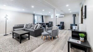 A modern living room with a sofa, armchair, coffee table, and a small side table with a plant. - Lakefront Muskoka Retreat 4 Bedroom Cottage  (MacTier)