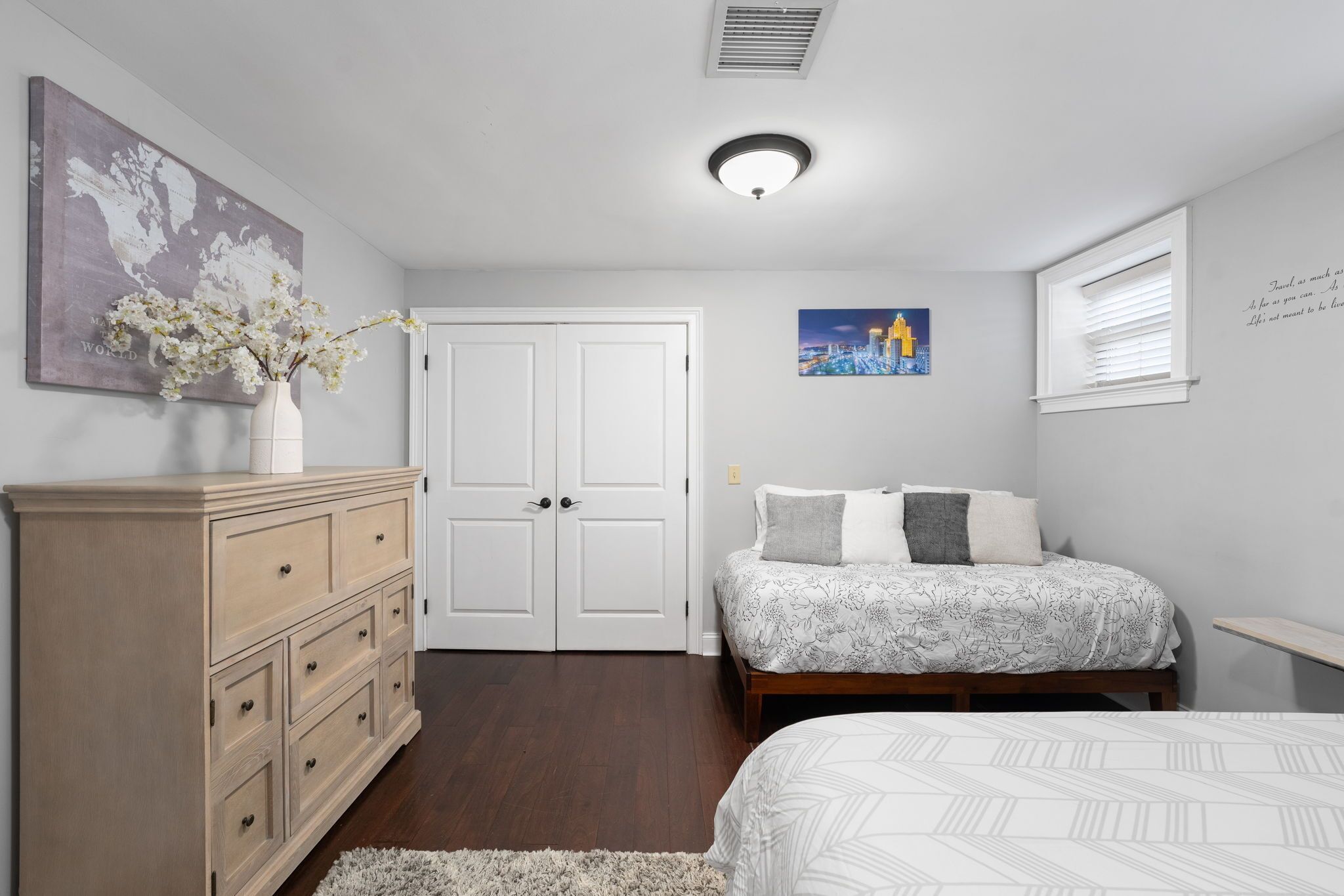 A bedroom with a bed, dresser, and a world map painting.