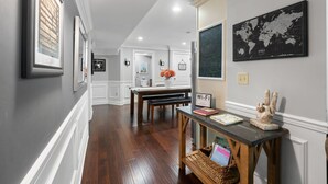Un couloir orné de tableaux encadrés, un banc en bois, une table avec un panneau indiquant la présence d’une connexion Wi-Fi et une carte du monde accrochée au mur.