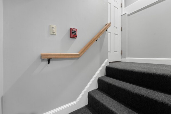 A staircase with a wooden handrail, a fire alarm, and a white door.