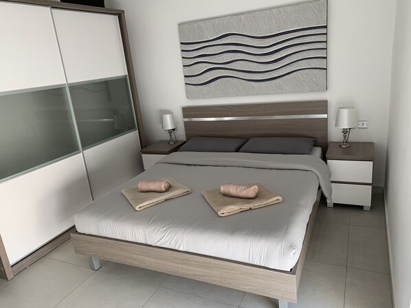 Un dormitorio moderno con cama, dos mesitas de noche, cabecero de madera, una obra de arte abstracta de gran tamaño y un armario con puertas correderas.
