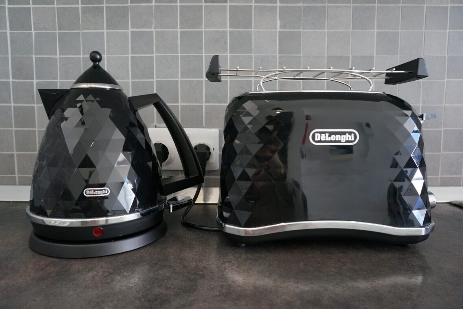 Two Delonghi espresso machines on a kitchen counter with a tiled backsplash.
