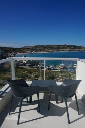 Balcón con dos sillas y una mesa, con vista a una zona costera con barcos y una playa.