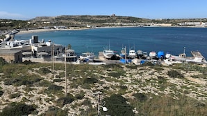 Ein Küstenhafen mit vertäuten Booten, einem Sandstrand und Gebäuden im Hintergrund.