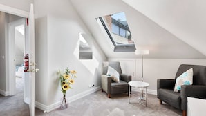A modern loft bedroom with a skylight, a sofa, a small table, and a vase of sunflowers. - Hampden Manor A Refined Battery Point Period Home (Battery Point)
