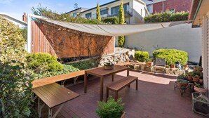 A patio area with wooden furniture, a table, and chairs, surrounded by potted plants and a decorative wall. - Hampden Manor A Refined Battery Point Period Home (Battery Point)