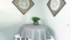 Un coin repas comprenant une table ronde, deux tabourets blancs, un ventilateur de plafond et deux assiettes décoratives fixées au mur.