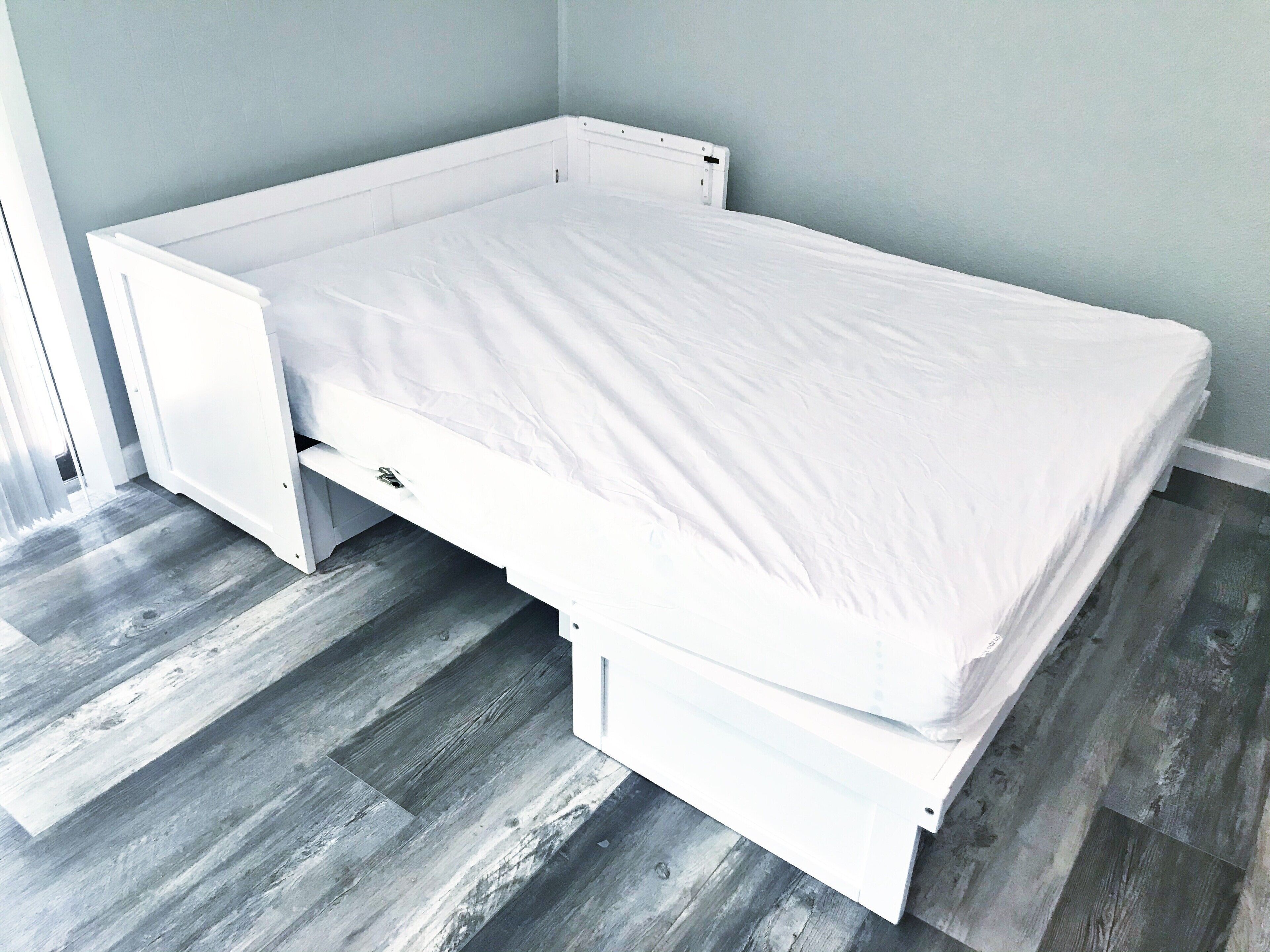 A white bed in a room with grey wooden flooring and light blue walls.