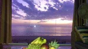Un frutero con fruta sobre una mesa, con vista al océano y al cielo a través de una ventana.