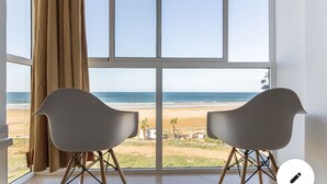 Habitación con un ventanal grande que da a la playa, dos sillas modernas y una cortina.