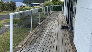 Une terrasse en bois avec une rambarde en verre, donnant sur une étendue d’eau et une montagne.