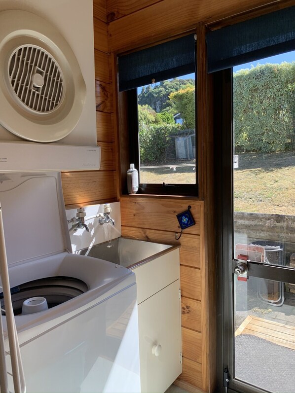 A compact bathroom with a washing machine, sink, and window with a view of greenery.