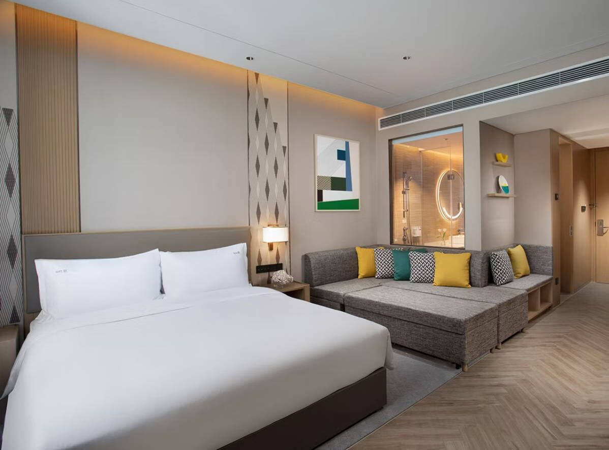 A hotel room with a large bed, a sofa, a mirror, and a wall with geometric patterns.