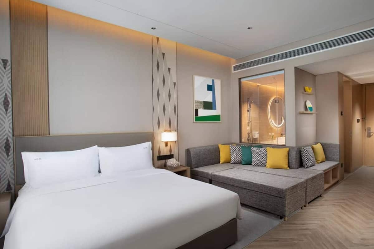 Ein Hotelzimmer mit einem großen Bett, einer Sitzecke, einem Spiegel und einer Wand mit geometrischen Mustern.