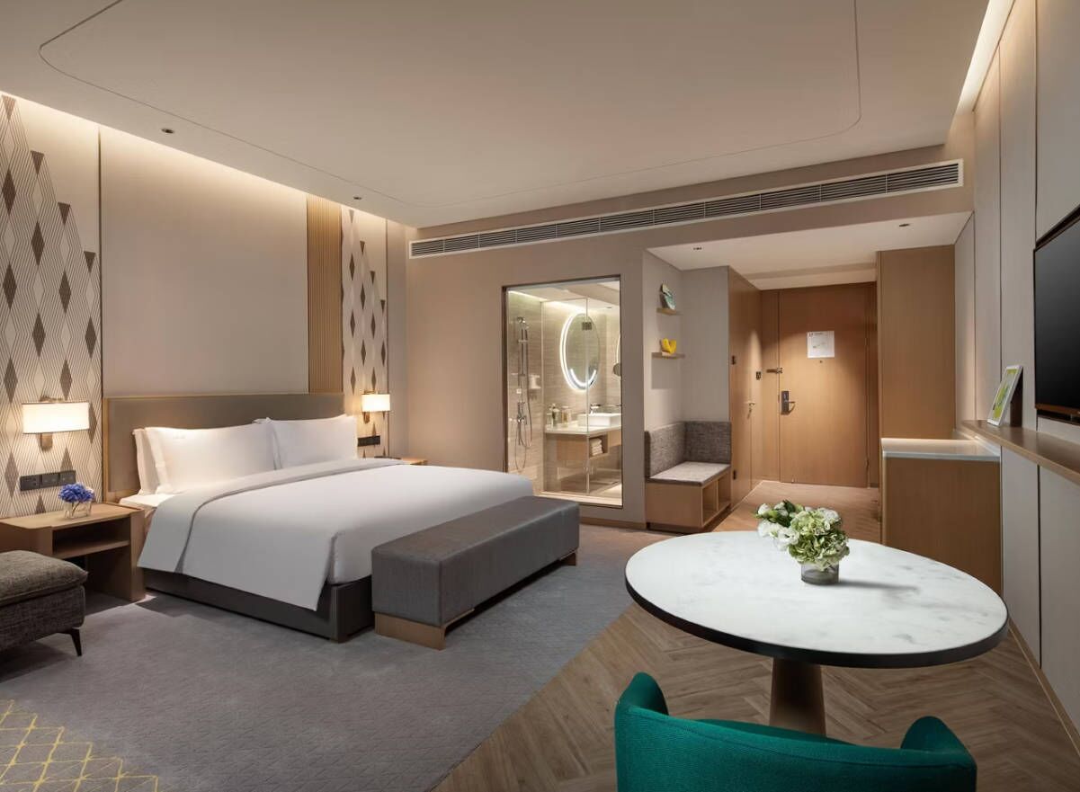 A modern hotel room with a large bed, bedside tables, a round dining table, and a TV.