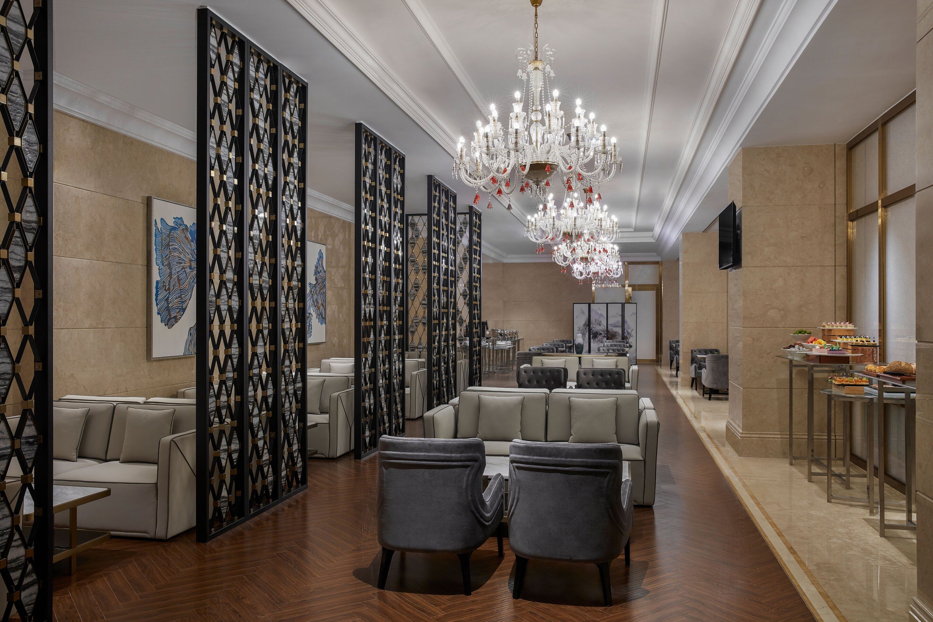 A spacious hotel lobby with a grand chandelier, seating areas, and a buffet setup.