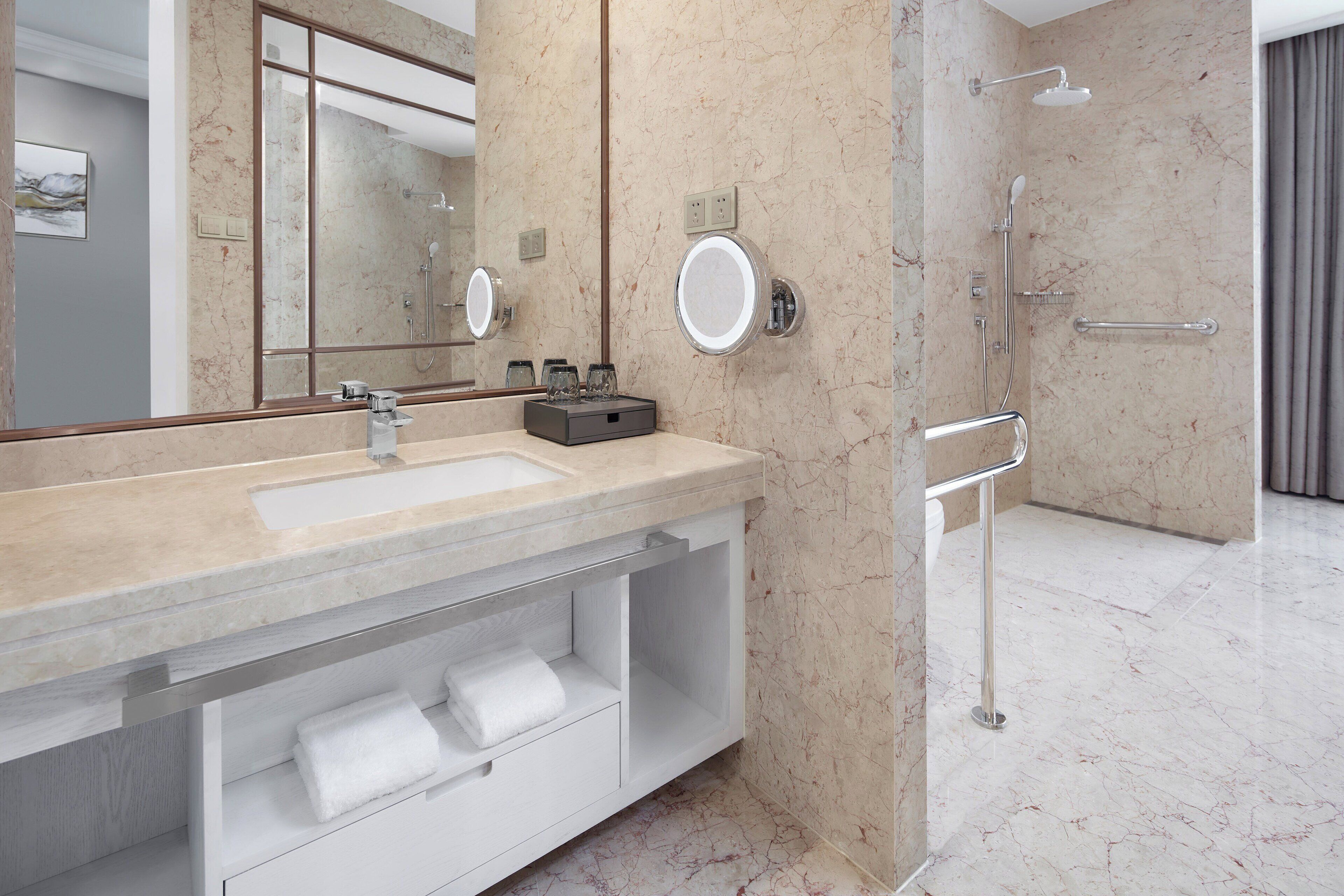 Een moderne badkamer met een marmeren wastafel, een grote spiegel, een douche met handdouche en een handdoekrek.