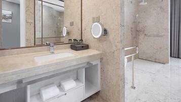 Een moderne badkamer met een marmeren wastafel, een grote spiegel, een douche met handdouche en een handdoekrek.