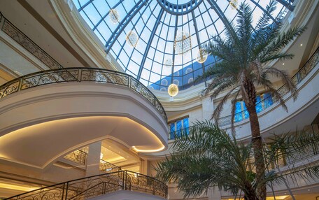 A multi-level atrium with a glass dome ceiling, palm trees, and ornate railings.
