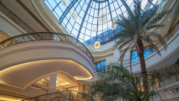 Un atrio de varios niveles con cúpula de cristal, palmeras y barandillas ornamentadas.
