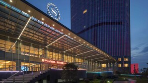 Un hotel moderno con una destacada torre de reloj, fachada de vidrio y una entrada bien iluminada.