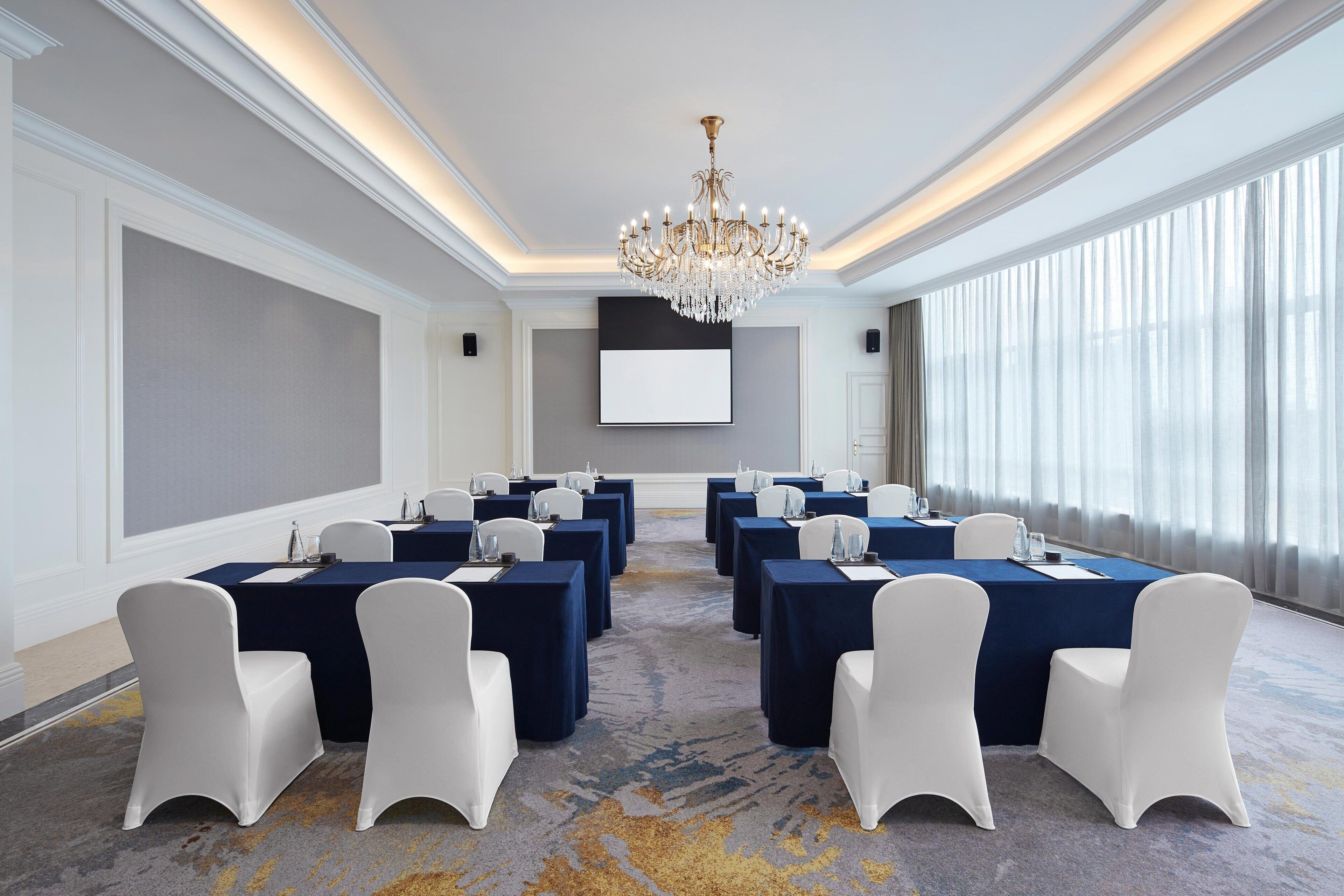 A conference room with a large screen, rows of tables, and chairs.