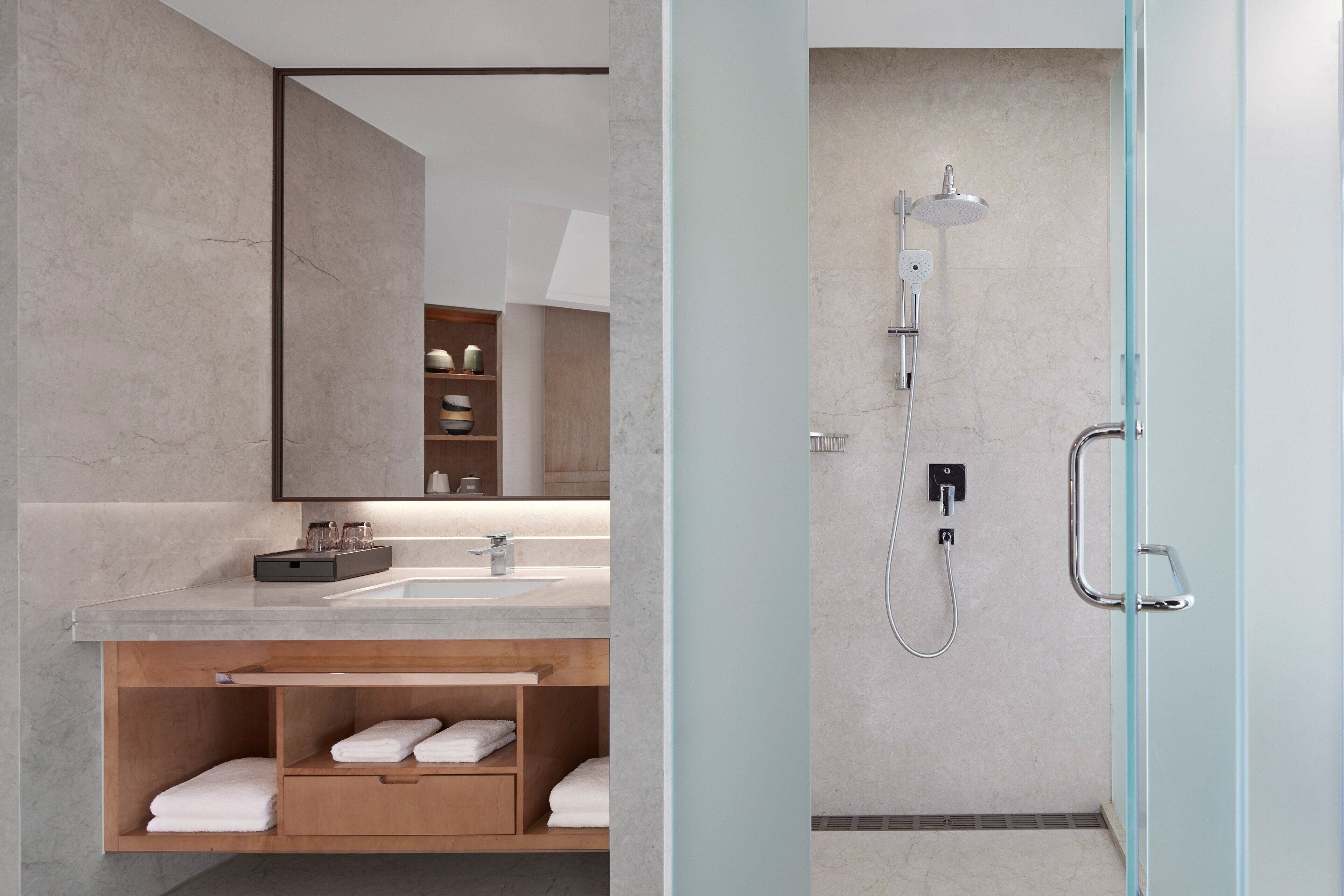 A modern bathroom with a marble sink, wooden vanity, and a glass-enclosed shower area.