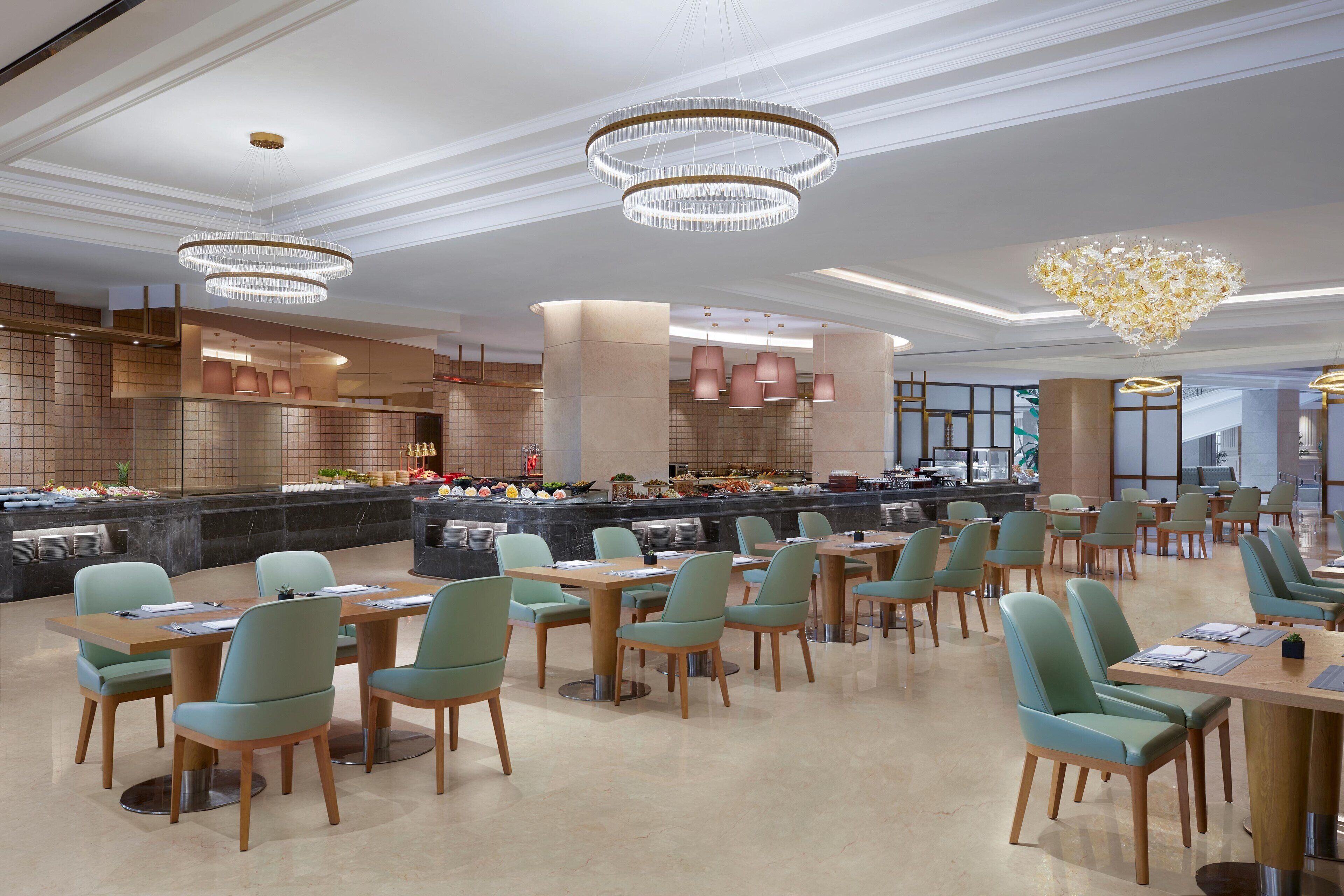 A modern dining area with multiple tables and chairs, a central buffet, and decorative lighting fixtures.