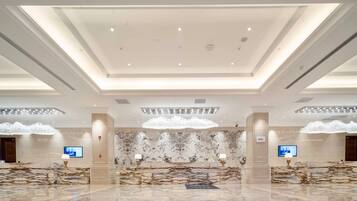 A spacious lobby with a marble reception desk, modern chandeliers, and a high ceiling with recessed lighting.