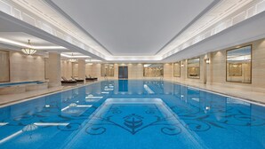 Una amplia piscina interior con un diseño decorativo central, rodeada de paredes con espejos grandes e iluminación empotrada.