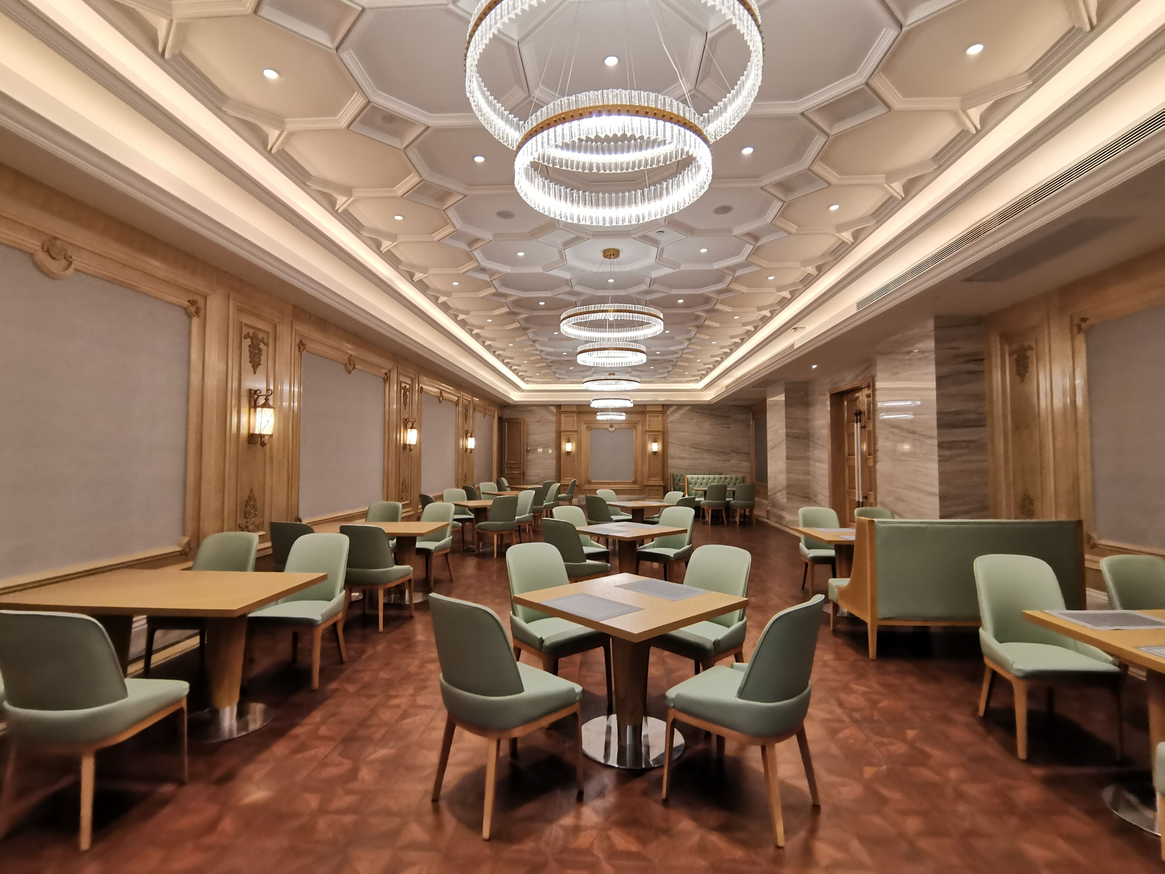 Un salón de conferencias espacioso con varias mesas y sillas, candelabros elegantes y un suelo de madera pulida.