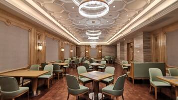 Un salón de conferencias espacioso con varias mesas y sillas, candelabros elegantes y un suelo de madera pulida.