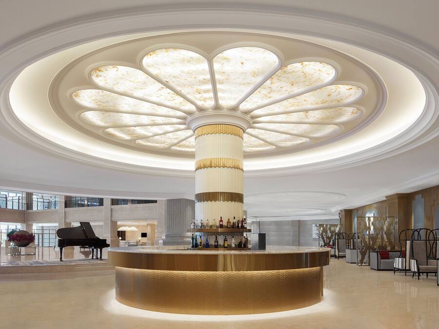 A grand lobby with a central bar, a grand piano, and a high ceiling with a decorative light fixture.