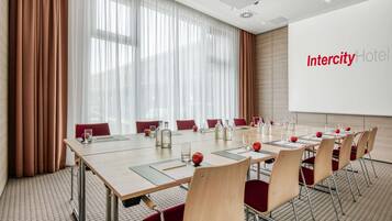 Une salle de conférence à l’hôtel Intercity, avec une longue table, des chaises rouges et un écran de projection.