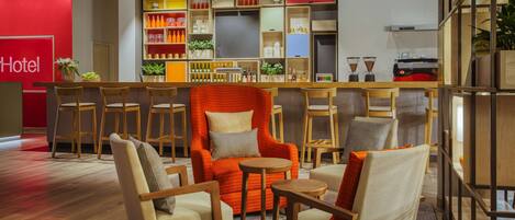 A hotel lobby with a red wall, wooden furniture, and a bar area with shelves of bottles and plants.