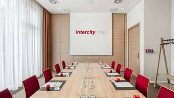 Un salón de conferencias con una larga mesa, sillas rojas y una pantalla de proyector que muestra 'Intercity Hotel'.