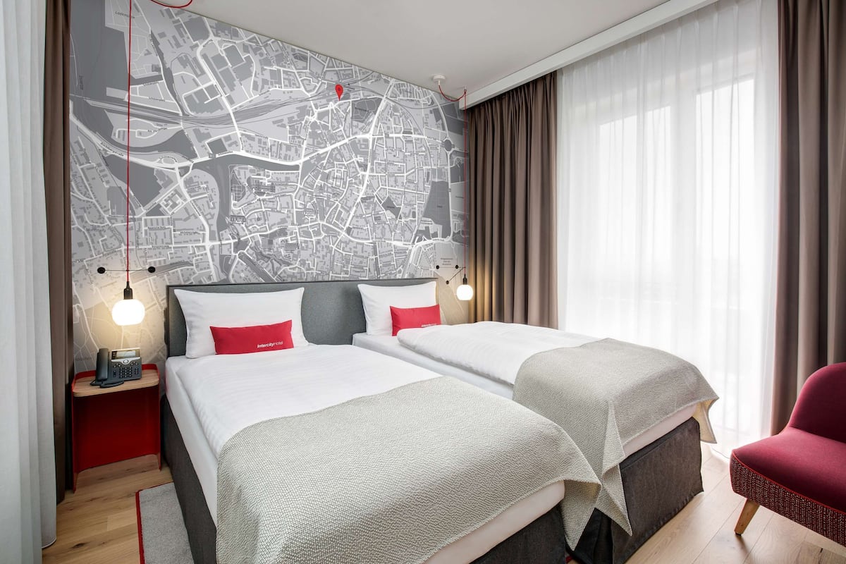 A hotel room with two beds, a map on the wall, a red chair, and a nightstand with a phone.
