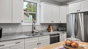 A modern kitchen with white cabinets, a stainless steel refrigerator, a granite countertop, and a window with a stained glass view.